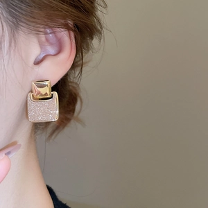 Close-up of 18k gold plated square earrings with shimmering sand surface on a model