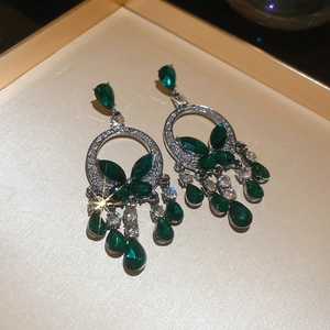 Detailed close-up of emerald green drop earrings with silver metal and butterfly accents