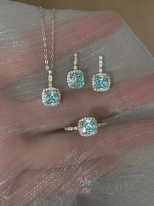 Macro detail of aquamarine jewelry set with necklace, ring and earrings on silver fabric