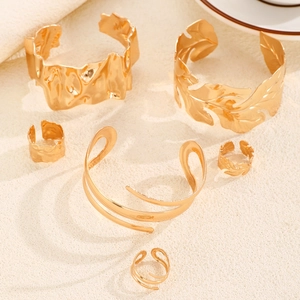 Conjunto de joyas doradas con brazaletes de hojas y anillos sobre fondo arena