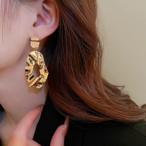 Detail view of large gold metallic irregular wave textured earrings on a model