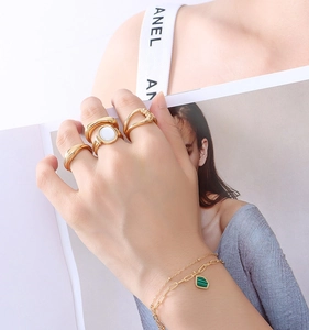 Detailed view of layered gold chain bracelet featuring a green emerald shield pendant