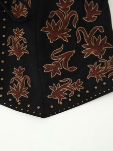 Détails de broderie sur gilet ethnique en daim noir avec des rivets en bronze