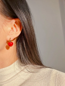 Close-up of red heart charm earrings with gold hoops worn on model for detail