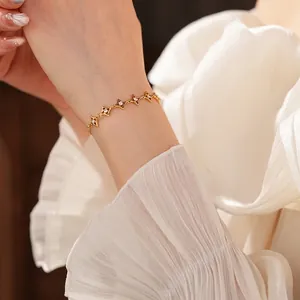 Bracelet plaqué or 18k avec breloques d'étoiles en zircon porté sur fond de tissu blanc