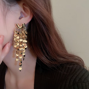 Detailed view of long gold tassel earrings with metallic sequins on a female model