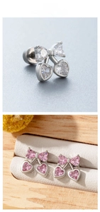 Detail of cherry stud earrings with bow and heart-shaped pink gems on wood display
