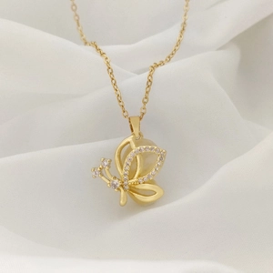 Macro detail of a golden butterfly pendant with sparkling crystals on white silk background