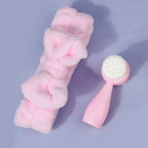 Close-up of a pink plush bow headband and a dual-sided silicone facial cleansing brush