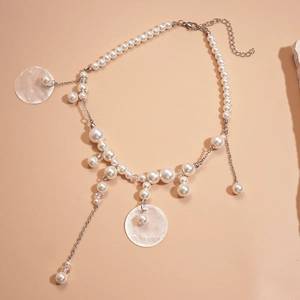 Detail of shell pendant and faux pearl tassel necklace with silver chain on apricot background