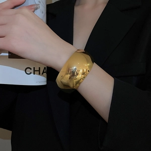 Detailed macro view of wide golden polished oval cuff bracelet on a fashion model wrist