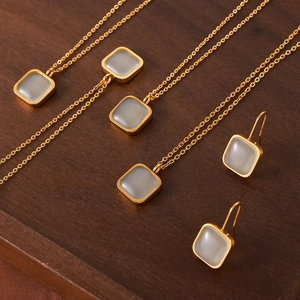 Minimalist gold necklace and earring set with grey resin stones on a wooden surface