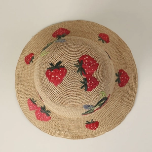 Detail of hand-woven straw hat featuring red strawberry embroidery and fine texture