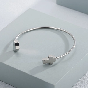 Silver stainless steel collar bangle featuring minimalist heart and cross charms on a pedestal