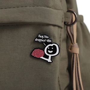 Funny cartoon brain enamel pin with 'Hey You dropped this' text on a green canvas bag