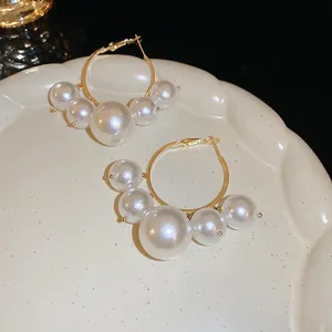 Golden hoop earrings with gradient oversized pearls on a white ceramic tray