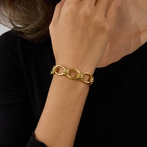 Close-up of gold interlocking circular link bracelet worn on a female wrist over black sleeve