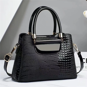 Detail of glossy black crocodile embossed leather handbag with elegant gold hardware