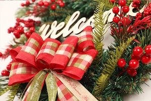 Close-up of Christmas wreath with red berries, welcome sign and Merry Christmas ribbon