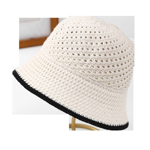 Detail of beige crochet bucket hat with black edge trim on a gold circular stand