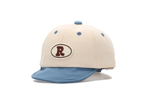 Détail de la casquette bébé avec visière contrastée et écusson brodé de la lettre R