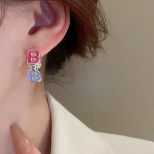 Close-up of silver huggie hoop earrings with pink and blue enamel letters and zircons