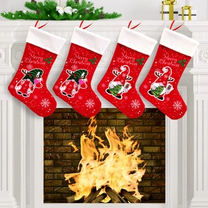 Detail of four red felt Christmas stockings with gnomes hanging on a warm fireplace