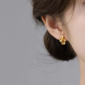 Detailed side view of a model wearing matte gold spiral wave clip-on earrings