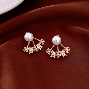 Dettaglio di orecchini a fiore placcati oro 14k con perle e motivi a croce su velluto