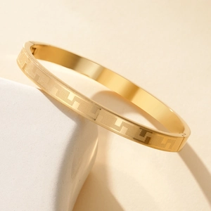 Minimalist gold titanium steel bangle with geometric pattern on stone display