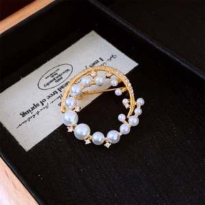 Detail of a 24k gold-plated pearl circle brooch with rhinestones on a jewelry box