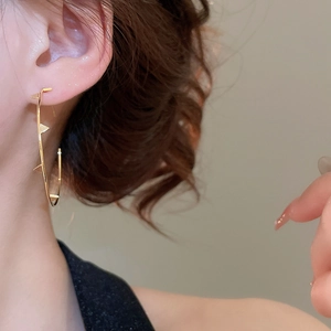 Close-up of golden triangular rivet earrings on model with polished metallic finish