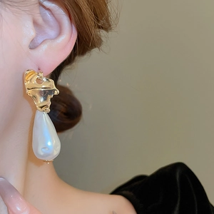 Close-up of irregular gold metal earring with a large baroque pearl on a female model