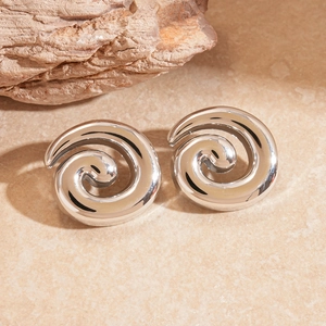 Macro detail of polished silver spiral earrings on a natural stone textured background