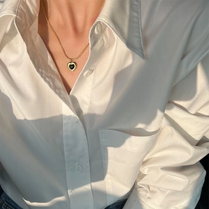 Golden snake chain necklace with black heart pendant worn on white shirt model