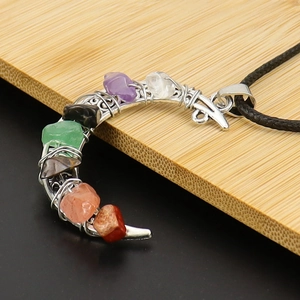 Close-up of crescent moon pendant with colorful chakra natural crystal stones on wood