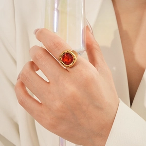 Dettaglio di un anello vintage dorato con zircone rosso quadrato e blazer elegante