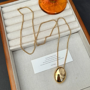 Golden teardrop pendant necklace on beige velvet display tray with elegant wood box