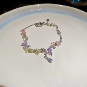 Detail of purple butterfly charm bracelet with colorful gravel stones on a white plate