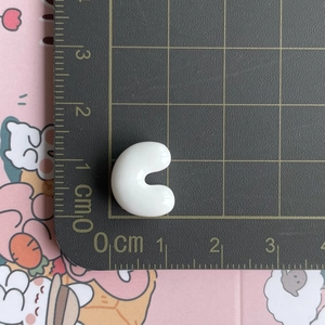 Macro detail of a small white resin letter C charm with metric scale ruler comparison