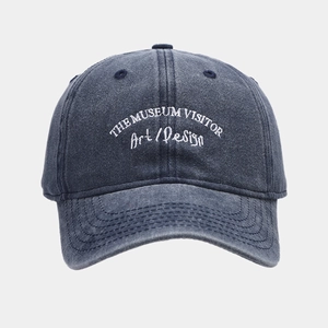 Detailed embroidery of THE MUSEUM VISITOR text on a washed denim baseball cap