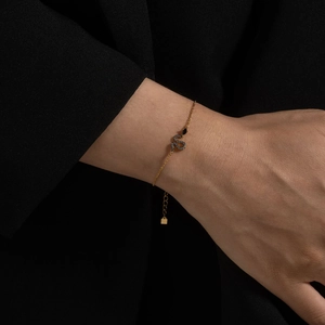 Detailed close-up of a gold snake pendant bracelet with black zircon on female wrist