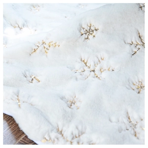 Detail of white faux fur Christmas tree skirt featuring golden sequin snowflake patterns