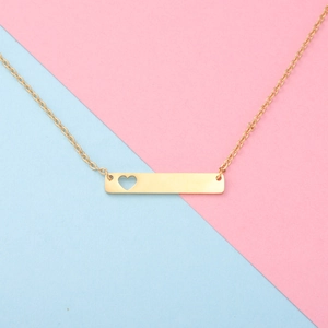 Close-up of golden rectangular bar necklace with a hollow heart on a pastel background