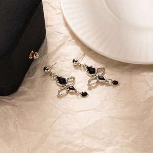 Détail de boucles d'oreilles gothiques en argent avec pierres noires sur fond beige