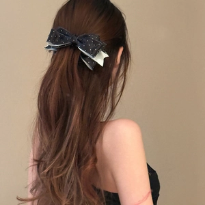 Elegant black polka dot bow hair clip shown on model with long wavy brown hair