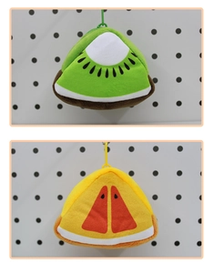 Close-up of kiwi and orange plush coin purses with hanging clips on a white board