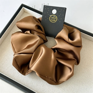 Detailed view of large brown satin scrunchie with handmade tag on a luxury display tray