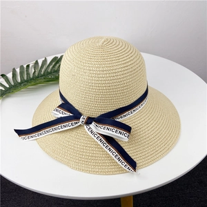 Détail d'un chapeau de paille beige avec ruban bleu, texte NICENICE et grand nœud