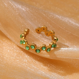Macro shot of gold-plated stainless steel ring with green zircon stones on pearly fabric